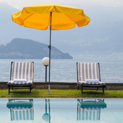 Vier Liegestühle vor dem beheizten Aussenpool des Hotel Beau Rivage mit einem gelben Sonnenschirm in der Mitte. Im Hintergrund der Vierwaldstättersee