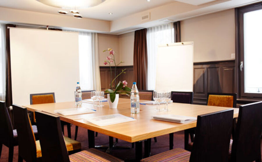 Seminarraum des Hotels mit grossem Tisch in der Mitte und Stühlen. Eine grosse Leinwand in der Ecke und ein Whiteboard daneben