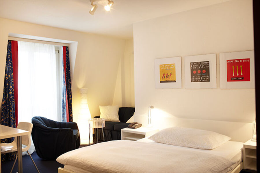 Gemütliches Budget-Zimmer mit grossem Bett, Teppich und modernen Gardinen. Zwei kleine Nachtlampen neben dem Bett